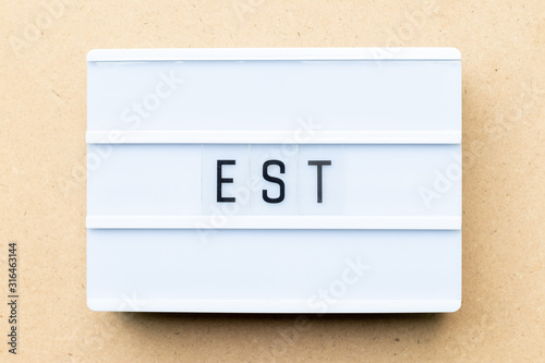 White lightbox with word est (abbreviation of established, estimated, eastern time zone, expressed sequence tag) on wood background