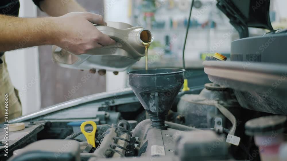 Car maintenance servicing mechanic pouring new oil lubricant into the car engine. Pouring fresh new clean synthetic oil into car engine. Change engine oil of your car.
