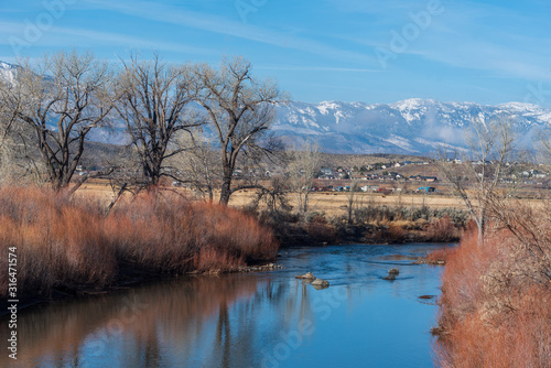 Landscape of the Carson River, bare trees, red reeds and snow-dappled mountains in the distance in Carson City Nevada