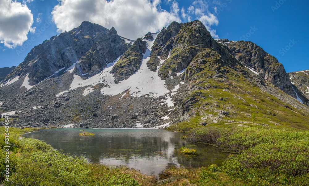 A small mountain lake. Rocky peaks and snowfields. Spring in the mountains.