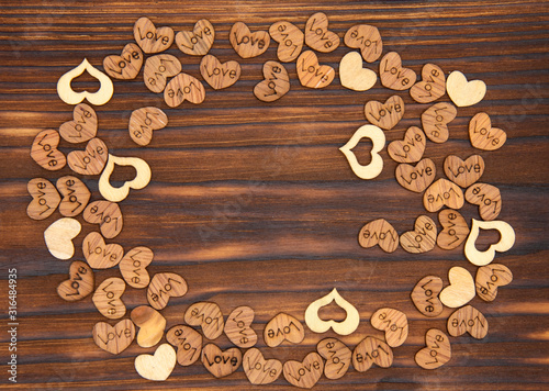 A frame of many wooden hearts on a dark wooden background.