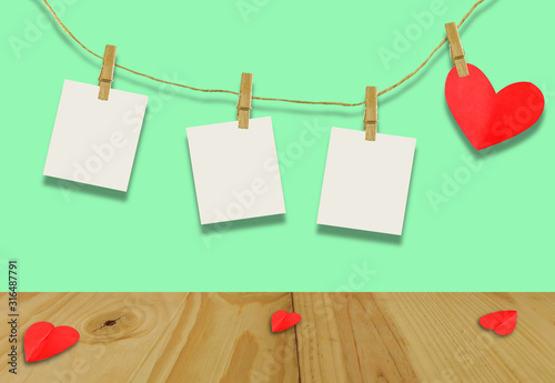The Valentine's day concept.A red heart shaped card attached to a wooden clip Hanging with hemp rope on pastel  green.Valentine's Day background