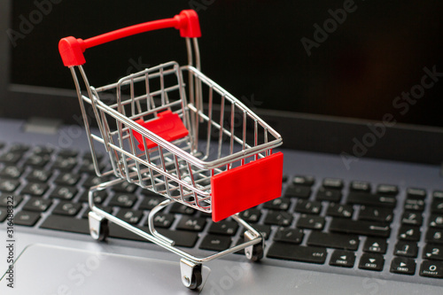 Small red shopping cart on silver laptop keyboard. Shopping online