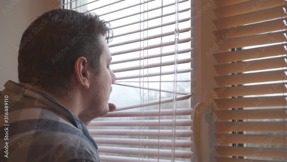 curious man looks out the window through the blinds curious man looks out the window through the blinds