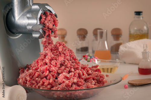 Minced meat comes out of a meat grinder against the background of glassware of a chemical laboratory. The manufacture of artificial meat. Close-up