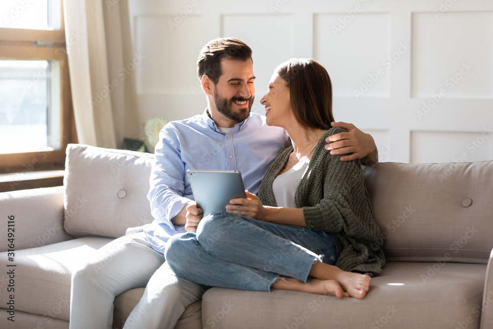 Millennial couple sit on couch surfing web on tablet Millennial couple sit on couch surfing web on tablet