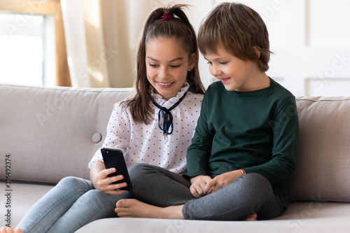 Cute little kids sit on couch using cellphone