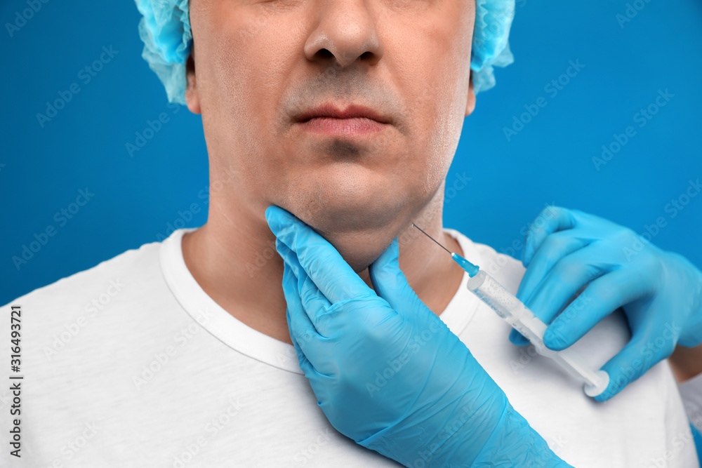 Mature man with double chin receiving injection on blue background, closeup Mature man with double chin receiving injection on blue background, closeup