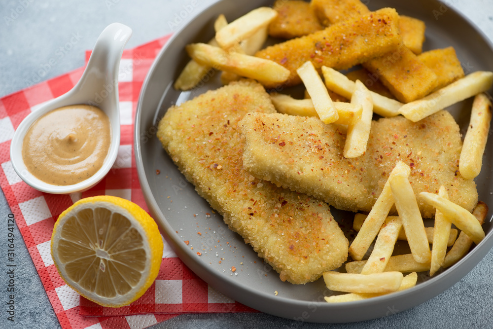 Roasted breaded fish fillet with french fries and lemon in a grey plate, close-up, selective focus Roasted breaded fish fillet with french fries and lemon in a grey plate, close-up, selective focus