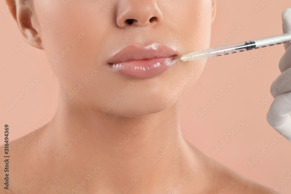 Young woman getting lips injection on peach background, closeup