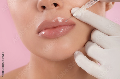 Fototapeta Young woman getting lips injection on pink background, closeup