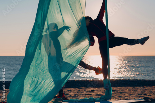 Two women practicing aerial yoga on the beach. Healthy Woman.