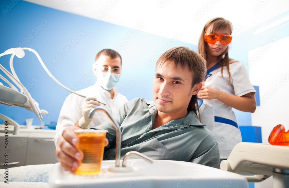 Young dentist doctor man in white uniform and special mask and young nurse woman examining man patient in dental office in clinic. Dental health and medical care concept Young dentist doctor man in white uniform and special mask and young nurse woman examining man patient in dental office in clinic. Dental health and medical care concept