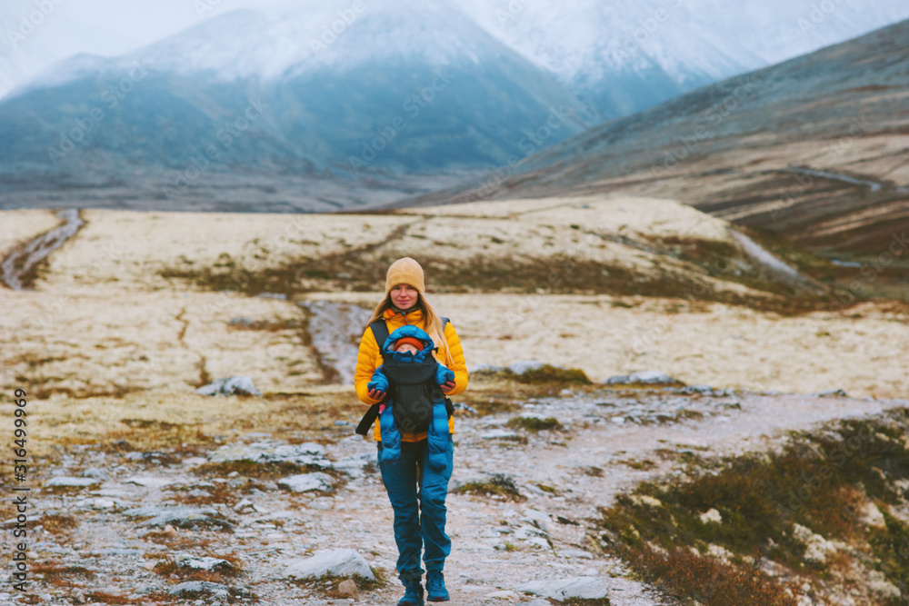 Fototapeta premium Mother with baby carrier hiking travel family healthy lifestyle woman and child active vacations outdoor in Norway mountain trail Rondane park.