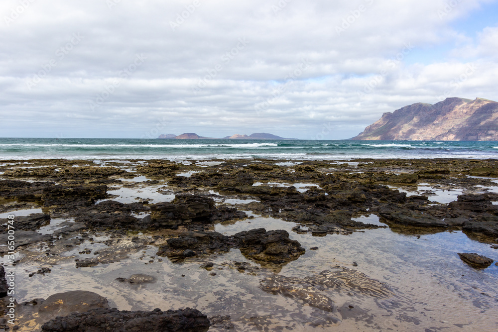 Coastline and sand beach Playa de Famara with mountain range and ocean waves in the north west of canary island Lanzarote