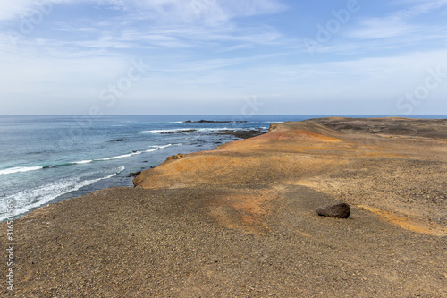Scenic view at the coastline in the natural park of Jandia (Parque Natural De Jandina) on canary island Fuerteventura with gravel, lava rocks and rough sea with waves