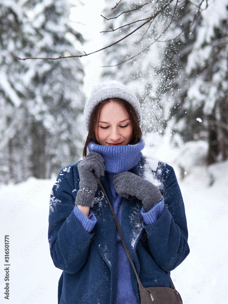 brunette walks through the winter forest in a gray hat, blue sweater and blue coat. brunette walks through the winter forest in a gray hat, blue sweater and blue coat.