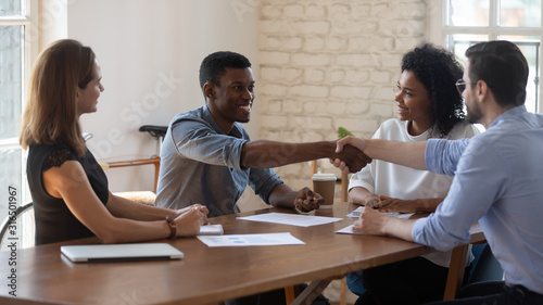 Happy diverse business partners shaking hands after successful negotiation