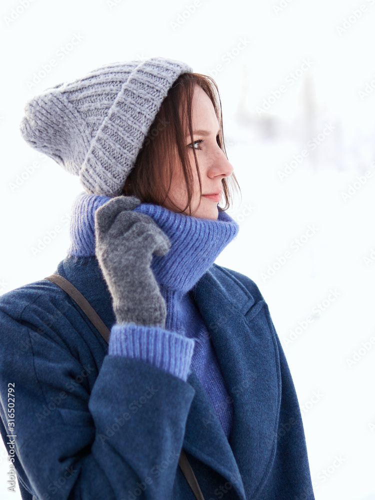 brunette walks through the winter forest in a gray hat, blue sweater and blue coat. brunette walks through the winter forest in a gray hat, blue sweater and blue coat.