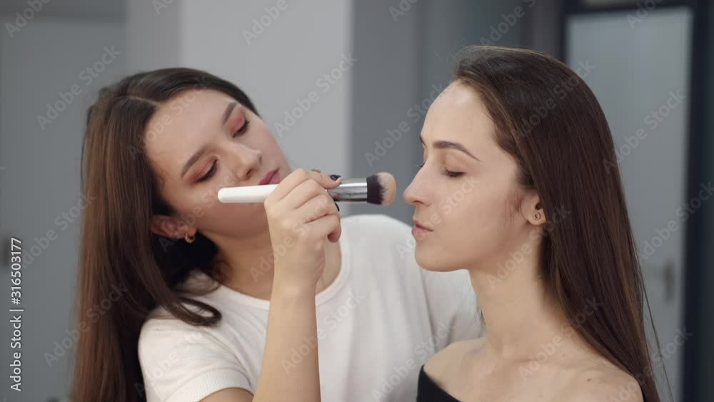 A client has brunette hair. An artist uses the brush. The girl is doing makeup for the young lady. A client has brunette hair. An artist uses the brush. The girl is doing makeup for the young lady.