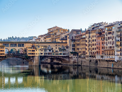 Florence in Italy in winter sunshine. The River Arno and part of the famous Ponte Vechio, Old Bridge, with unidentifiable tourists, in January 2020.