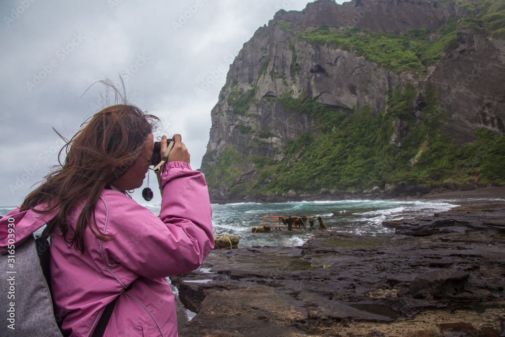 A travel lady are taking picture of the amazing beautiful landscape view of SeongSan Ilchulbong (Volcanic Cone) in Jeju Island,South Korea