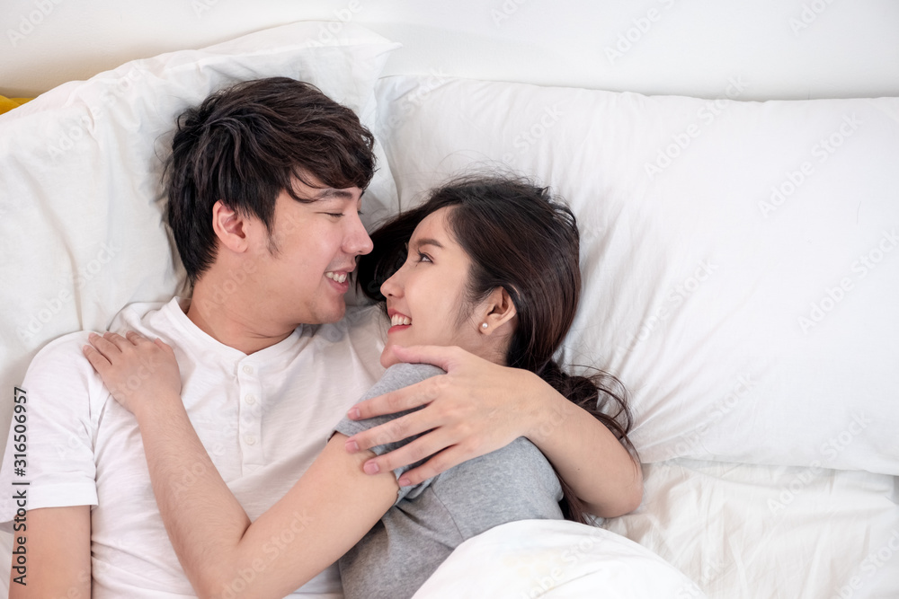 Top view lovely young Asian couple laying and hugging together on bed in bed room Top view lovely young Asian couple laying and hugging together on bed in bed room