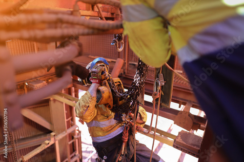 Rope access rigger wearing full body safety harness hardhat abseiling standing fall arrest position lifting 2 tone chain black clipping into D shackle lifting lug 