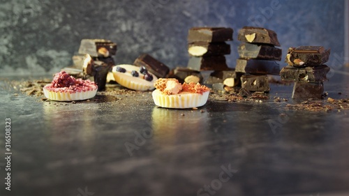 pieces of dark chocolate with nuts and white chocolate candies decorated with berries on a black background