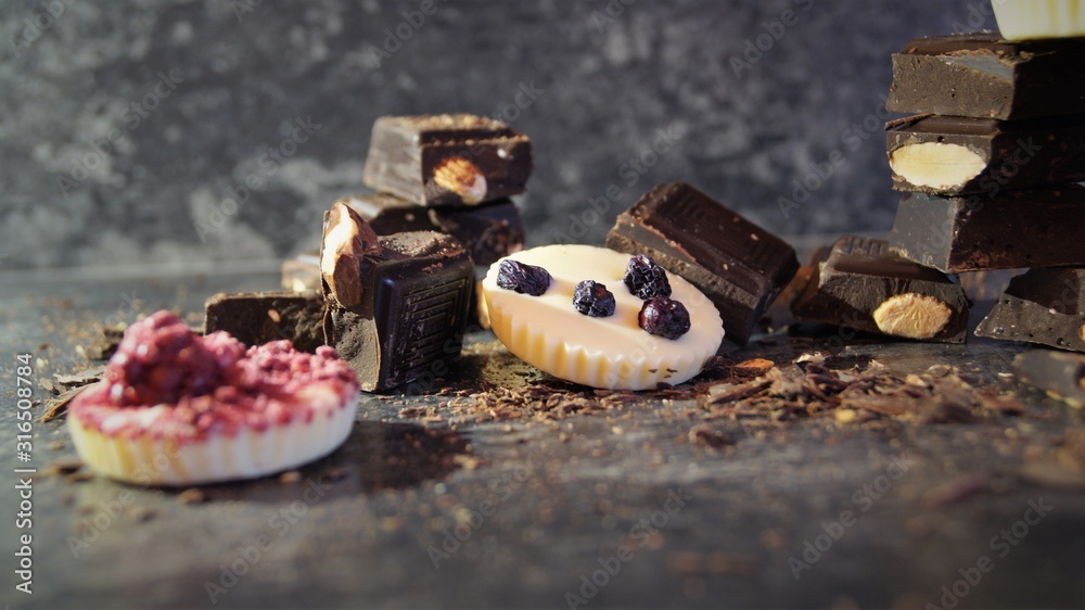 pieces of dark chocolate with nuts and white chocolate candies decorated with berries on a black background pieces of dark chocolate with nuts and white chocolate candies decorated with berries on a black background