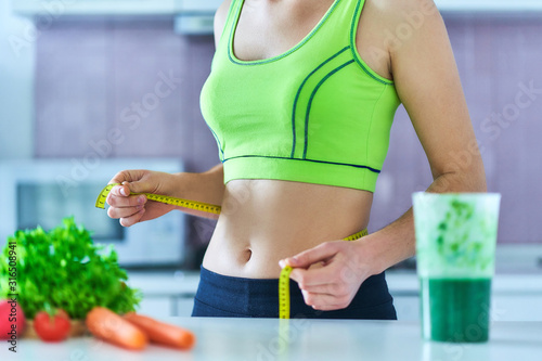 Diet woman in sportswear with measuring tape and a green smoothie for losing weight. Vegetables detox organic fitness drinks for healthy eating