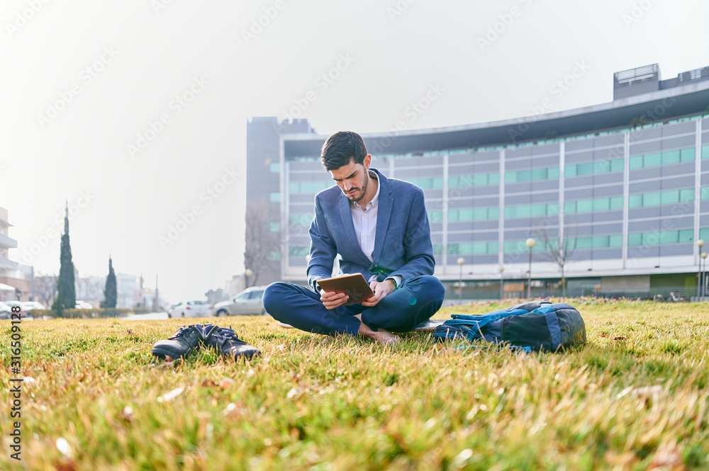 young businessman using a tablet sitting barefoot on a lawn in front of the business center young businessman using a tablet sitting barefoot on a lawn in front of the business center