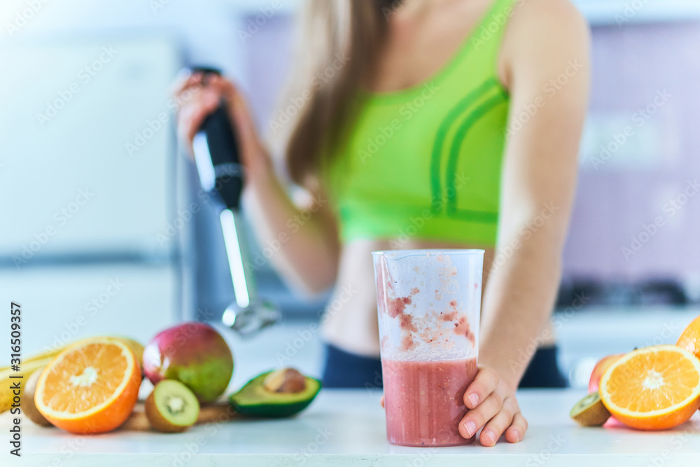 Healthy fitness woman in sportswear prepares a fresh fruit smoothie using a hand blender at home in the kitchen. Vitamin diet drinks