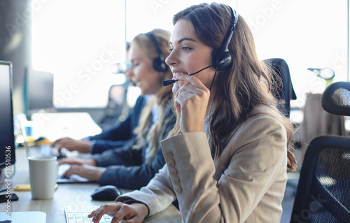 Female customer support operator with headset and smiling, with collegues at background. photo