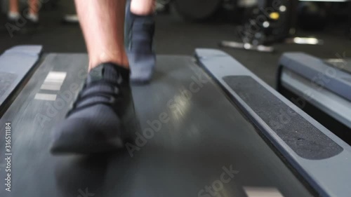 Man's feet in the black sneakers running on a treadmill in the gym. Front low angle