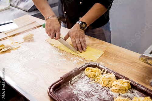 Chef rolling dough with a pasta machine. Pasta maker machine. Homemade italian style cuisine. Restaurant.