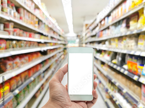 Hand holding smart phone or mobile phone on convenience store shelves interior blur background , Blur Supermarket shelves 