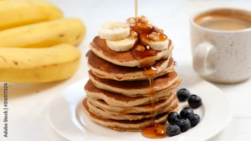 Pouring maple syrup on stack of pancakes in a slow motion. Tasty breakfast food, white table background. Sweet golden syrup pouring on pancakes Pouring maple syrup on stack of pancakes in a slow motion. Tasty breakfast food, white table background. Sweet golden syrup pouring on pancakes
