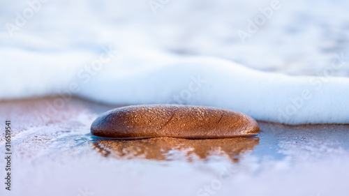 Sand covered stone being washed by gentle surf on a sandy beach