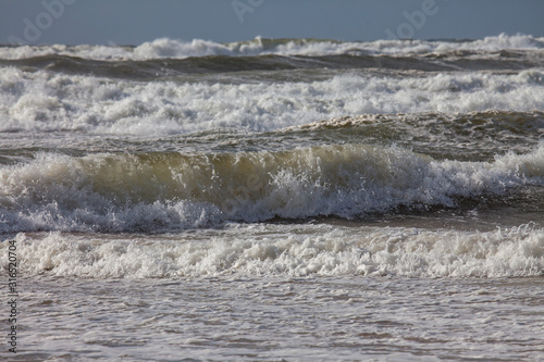 Принти на полотні Waves of the north sea with white spindrift in front of a blue sky