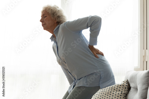 Unhappy older woman feeling pain, touching lower back