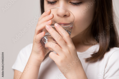 Close up little healthy girl drinking glass of pure water.