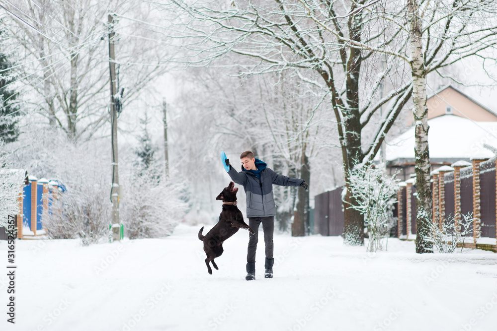 A boy walks with his brown labrador in the village on a snowy day