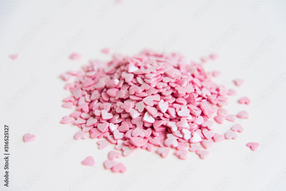 Fototapeta premium A lot of small heart-shaped candies, piled up on a light background. Pink pills. The concept of sweet love. Concept. Lots of hearts.