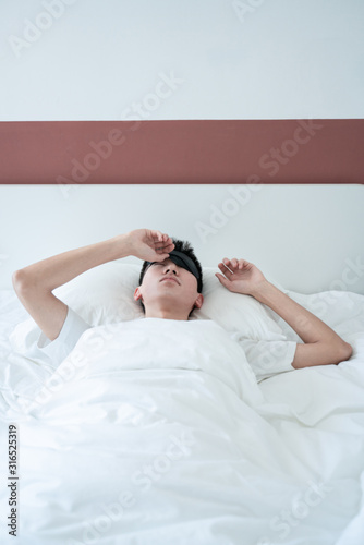 asian young man sleeping in bed with an eye mask in bedroom