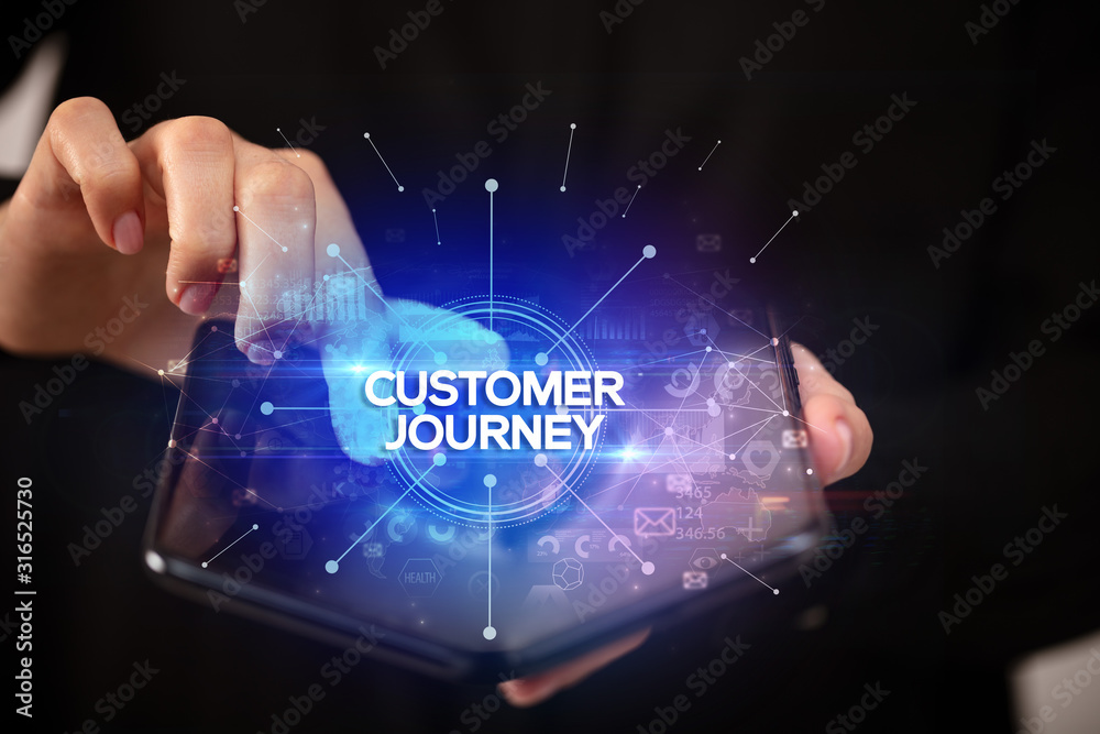 Businessman holding a foldable smartphone with CUSTOMER JOURNEY inscription, new business concept Businessman holding a foldable smartphone with CUSTOMER JOURNEY inscription, new business concept