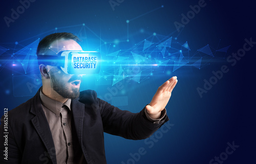 Businessman looking through Virtual Reality glasses with DATABASE SECURITY inscription, cyber security concept