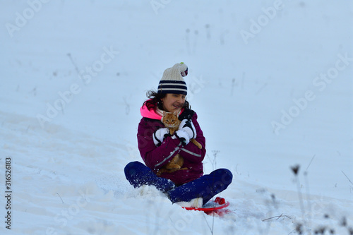 Girl sledding downhill on snow in winter and laughing with joy
