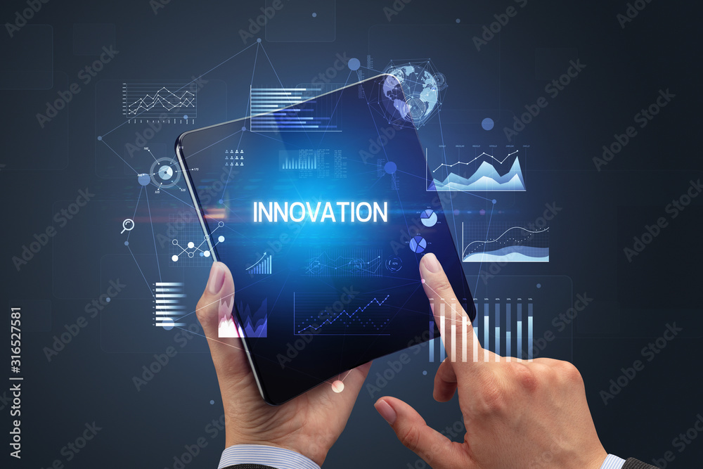 Businessman holding a foldable smartphone with INNOVATION inscription, successful business concept Businessman holding a foldable smartphone with INNOVATION inscription, successful business concept