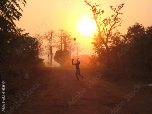 Silhouette of african kid playing with ball in sunset light in the far remote wilderness of southern Tanzania